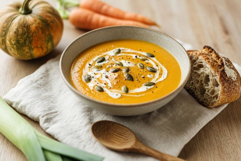 Bol de velouté de potiron et carottes maison aux graines de courge, avec du pain de campagne et des légumes d’automne